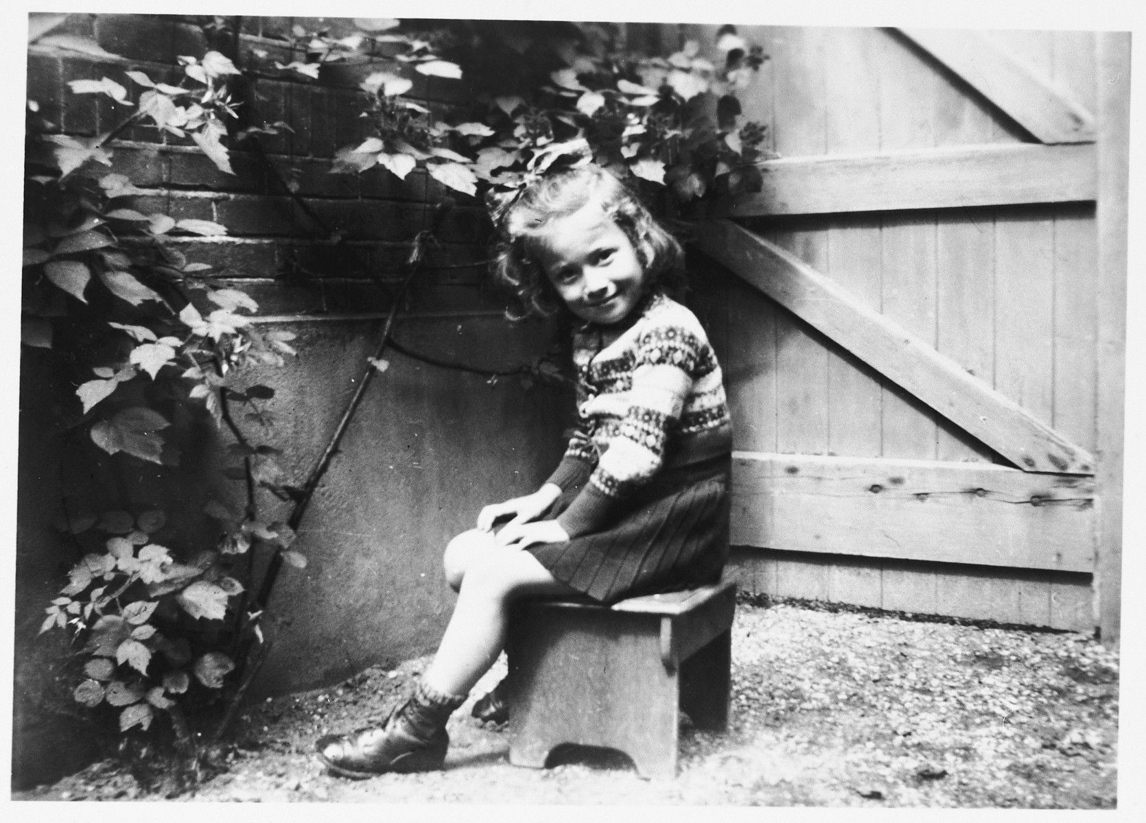 A young Jewish child sits in the garden of her Dutch rescuers' home wearing a sweater made by her mother prior to her deportation.

Pictured is Truusje Schoenfeld just before leaving the home of her rescuers to return to Amsterdam after the war.