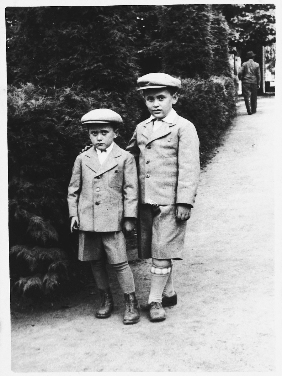 Two young Jewish brothers wearing matching suits and caps pose next to a hedge in Jaroslaw, Poland.

Pictured are Maurice and Shimon Friedberg.