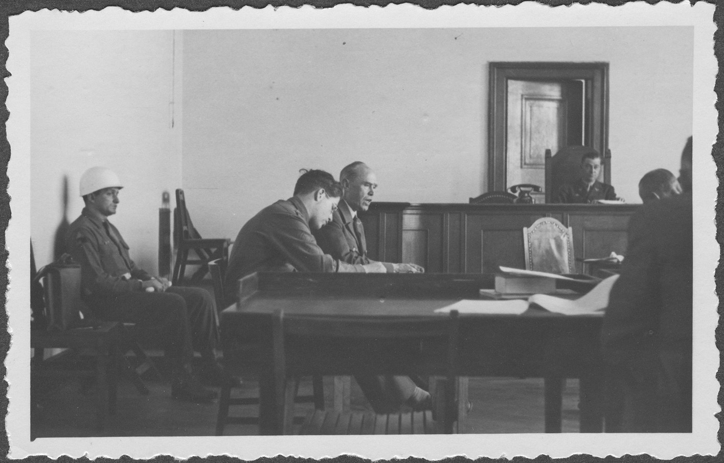 Interrogation of German Field Marshall Albert von Kesselring at the IMT Nuremberg commission hearings investigating indicted Nazi organizations.  
An interpreter sits beside Kesselring and an armed guard sits behind him.  In the background is Commissioner Taylor.