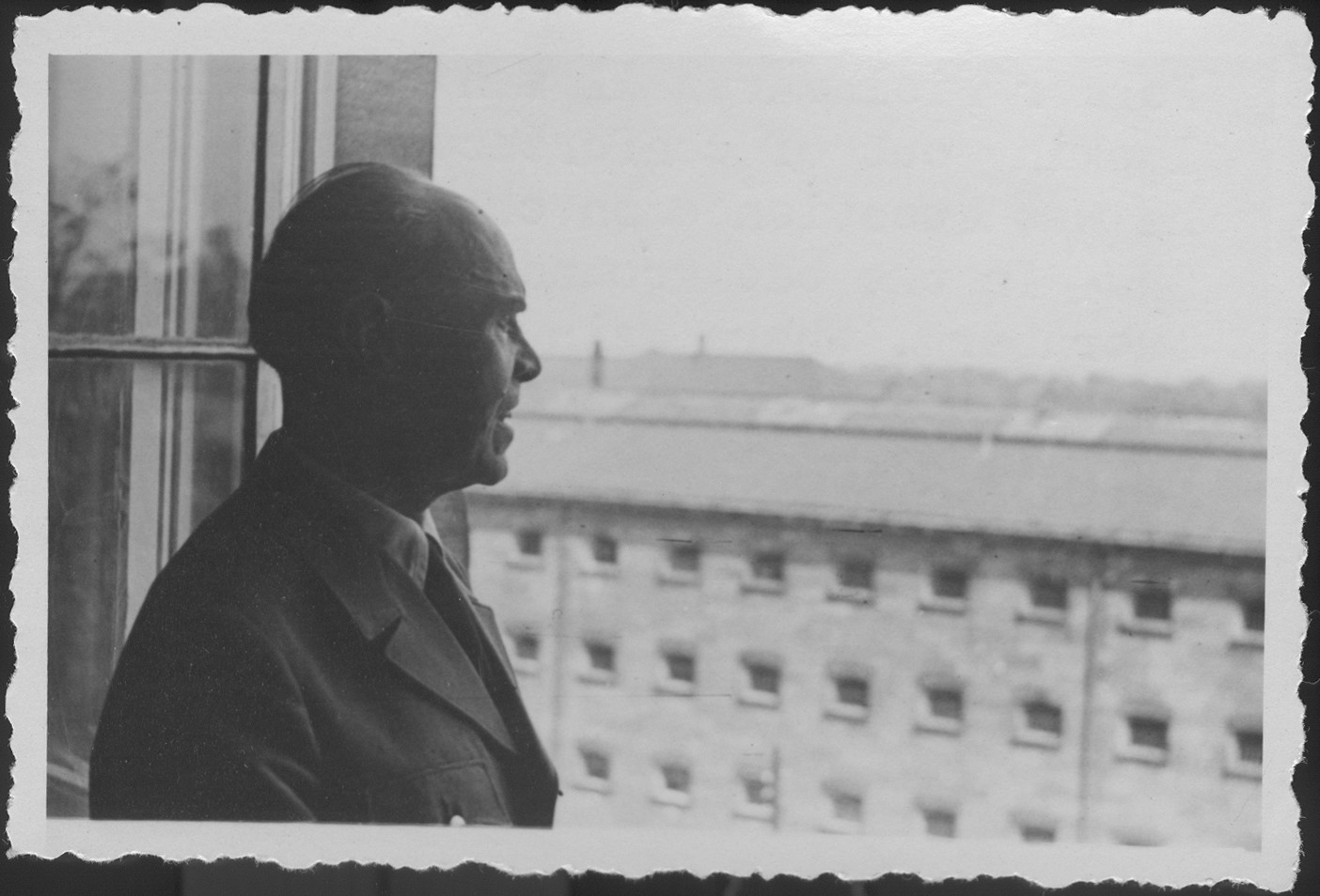 Former German Field Marshall Albert von Kesselring looks out of the window of the conference room where he was being questioned during IMT Nuremberg commission hearings on the Supreme Command of the German Armed Forces, OKW.

In the background is the Nuremberg prison where the IMT defendants were kept during the trial.