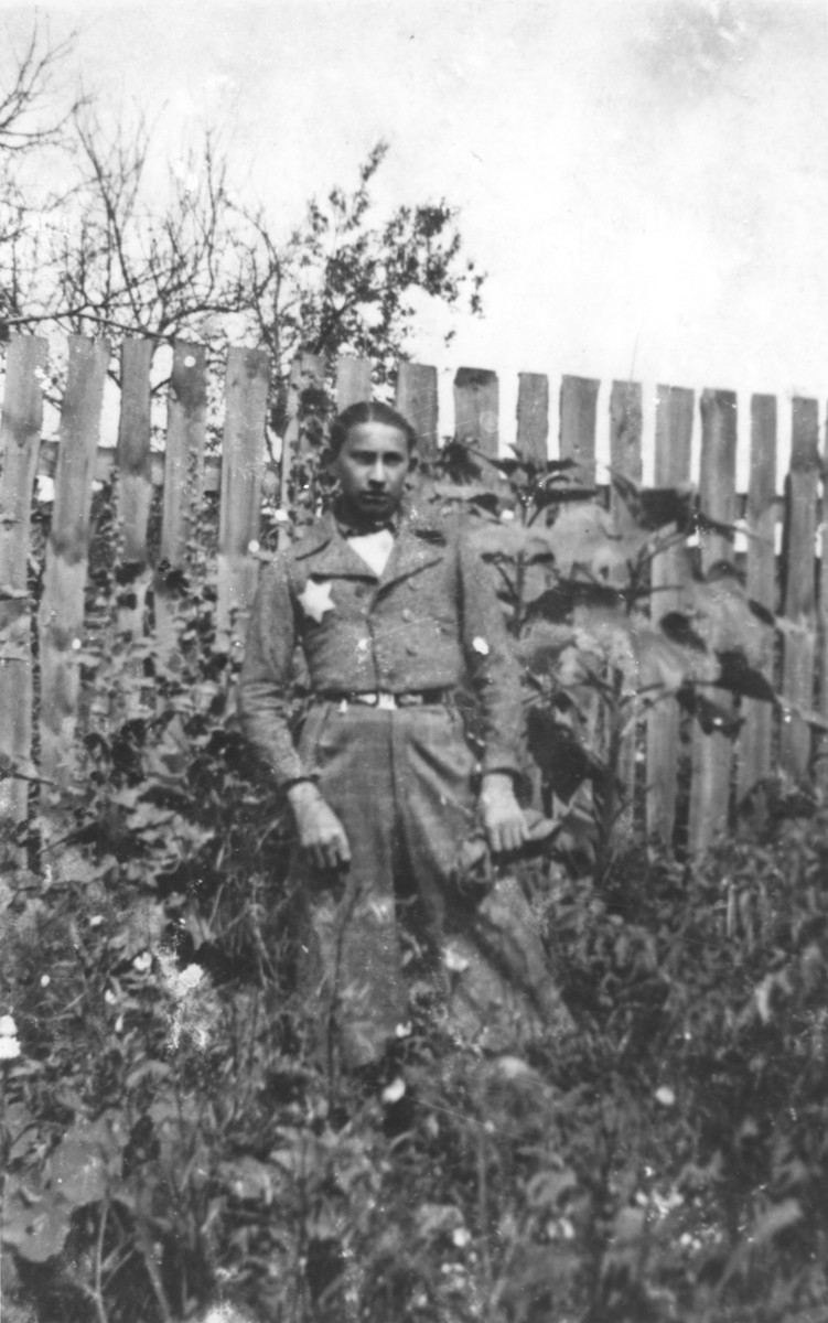 A youth wearing a Jewish badge poses in front of a wooden fence in Ozorkow, Poland.

Pictured is 15-year-old Moshe Rosenkrantz.