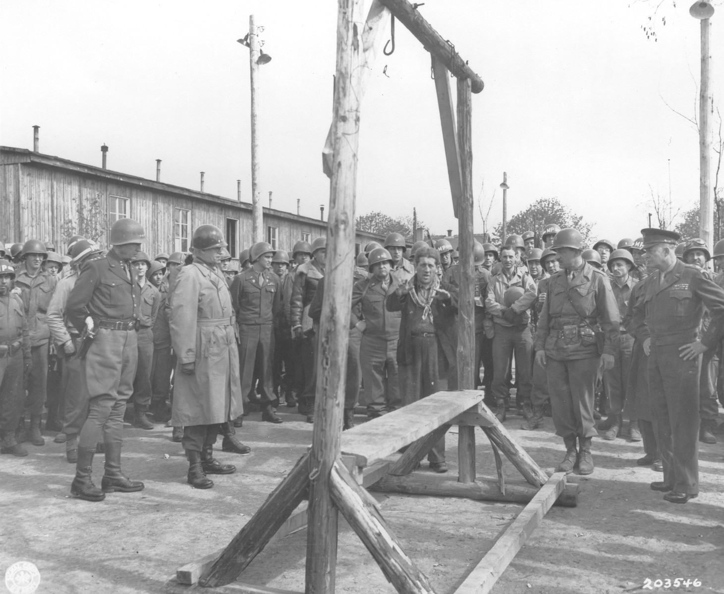 An Austrian-Jewish survivor, who had been deported from Holland, points out the gallows in Ohrdruf to General Dwight D. Eisenhower and a party of high ranking U.S. officers, including General Omar N. Bradley, Lt. Gen. George S. Patton, and Major General Troy H. Middleton, during an official tour of the newly liberated concentration camp.

The Austrian Jewish survivor is Ignaz Feldmann (wearing a dark coat, with a scarf around his neck) . He was a survivor of  Westerbork, Terezin, Auschwitz, and Ohrdruf camps.   He was also a player on the famed Hakoah Vienna soccer teams of the 1920s and 30s.