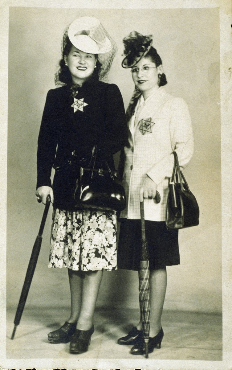 Two well-dressed women wearing Jewish stars pose holding umbrellas.

Pictured on the right is Simone (Grynberg) Finifter.  The photo, which is inscribed to her daughter, Rachel, reads: "Your mother, who suffers a lot."