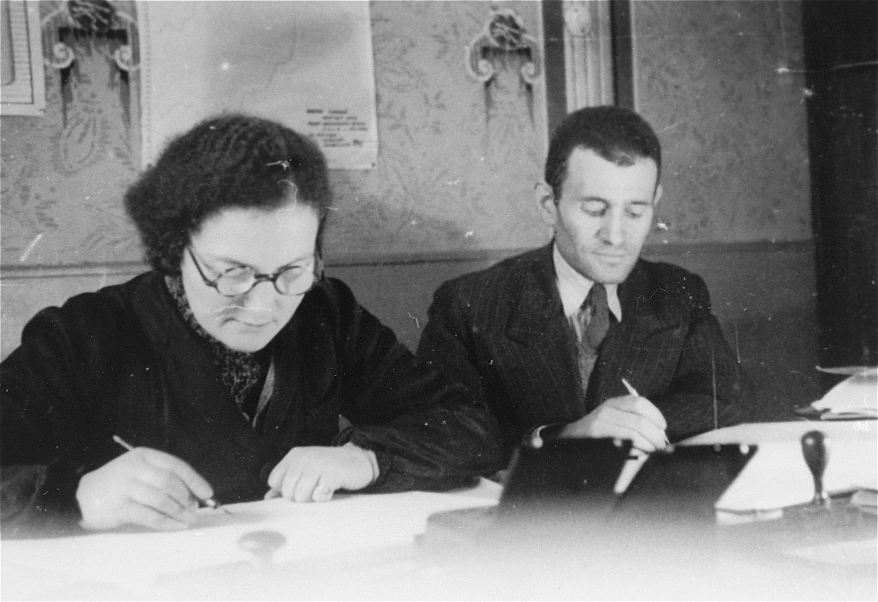 Members of the ghetto administration sit  at a table in the office of the Judenrat in the Kielce ghetto.

This photo was one the images included in an official album prepared by the Judenrat of the Kielce ghetto in 1942.