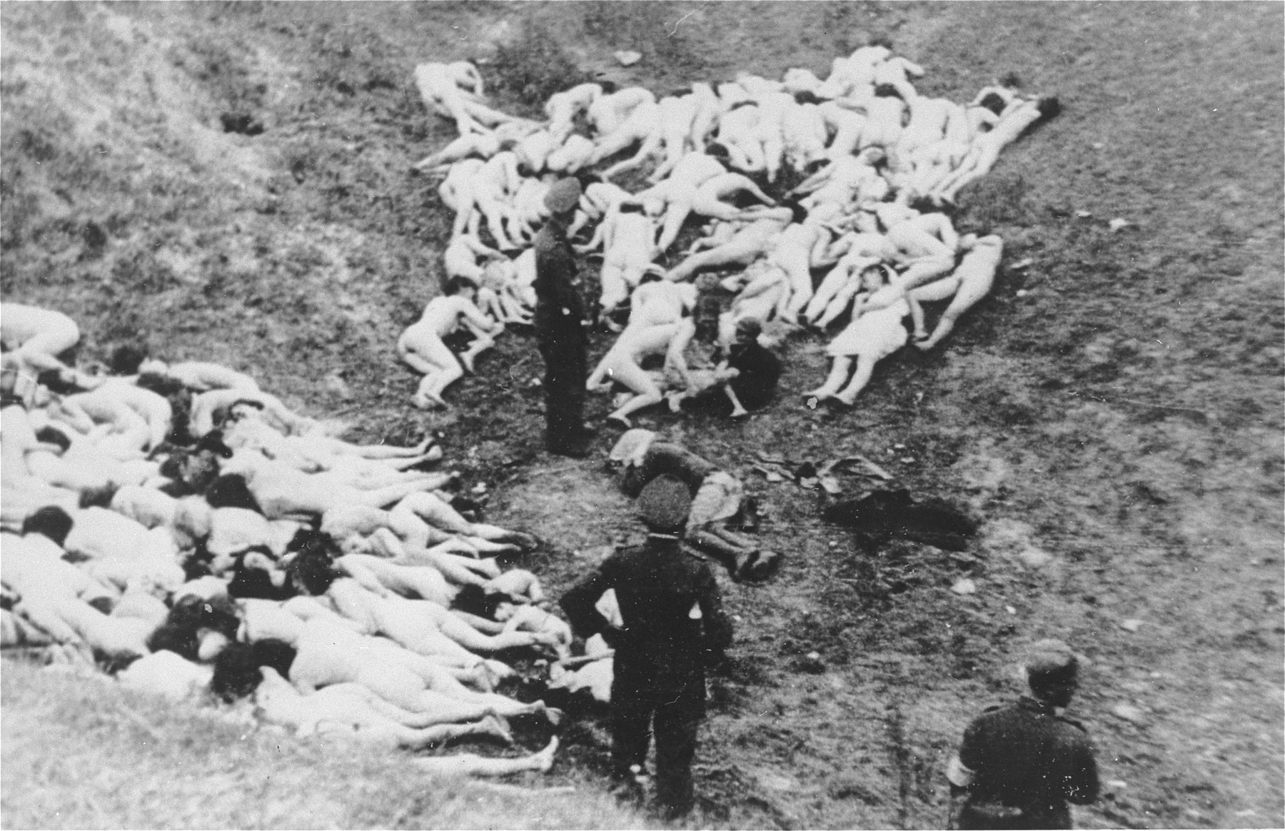 A German policeman prepares to complete a mass execution by shooting two Jewish children, who were shot with the others in connection with the liquidation of the Mizocz ghetto.

According to the Zentrale Stelle in Germany (Zst. II 204 AR 1218/70), these Jews were collected by the German Gendarmerie and Ukrainian Schutzmannschaft during the liquidation of the Mizocz ghetto, which held roughly 1,700 Jews.  On the eve of the ghetto's liquidation (13 October 1942), some of the inhabitants rose up against the Germans and were defeated after a short battle.  The remaining members of the community were transported from the ghetto to this ravine in the Sdolbunov Gebietskommissariat, south of Rovno, where they were executed.  Information regarding this action, including the photos, were acquired from a man named Hille, who was the Bezirks-Oberwachtmeister of the Gendarmerie at the time.  Hille apparently gave the five photos (there were originally seven) to the company lawyer of a textile firm in Kunert, Czechoslovakia, where he worked as a doorman after the war.  The Czech government confiscated the photos from the lawyer in 1946 and they subsequently became public.  That the photos indeed show the shooting of Jews in connection with the liquidation of the ghetto was also confirmed by a statement of Gendarmerie-Gebietsfuehrer Josef Paur in 1961.