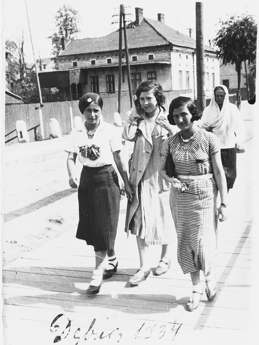 Three young Jewish women walk along a street in Debica, Poland.

Pictured from left to right are: Regina Hollender, Susi Hollender and Helena Fisz.