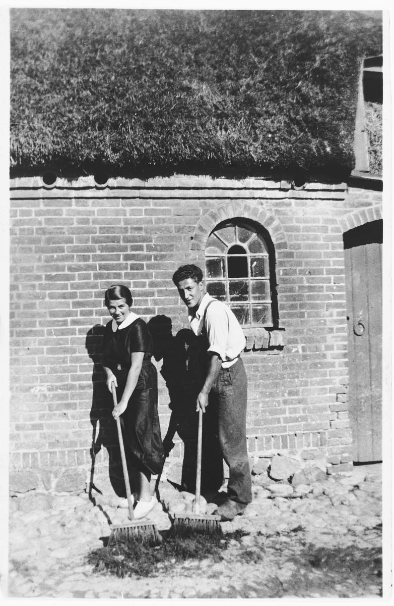 A young Jewish refugee from Germany sweeps outside with his girlfriend on a farm in the Jutland, where members of his hachshara [Zionist collective] are living.

Pictured are Josef Geldmann and Kaja Diament.