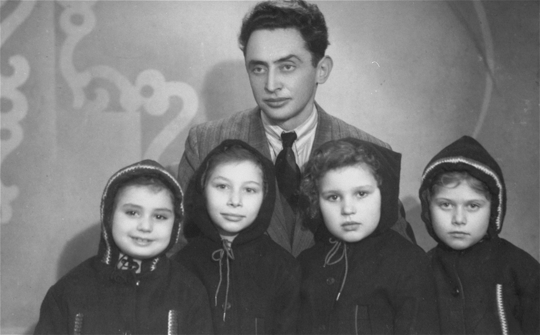 Jehuda Bornstein poses with four Jewish girls he retrieved from hiding and placed in a children's home on Narutowicza Street in Lodz. 

Pictured from left to right are: Halinka, who was hidden as Zinaida Bar in Legnica, Poland by a Christian woman whose name was Ostrowska; Wandeczka, now known as Tamy Lavee, who had been hidden by a Christian woman; Basia David, who was hidden in Orlovo by the Polubinska family who treated Basia so well that she didn't want to leave them; and Sabina (Inka) Kagan, hidden by the Roztropowicz family in Nidzica.
