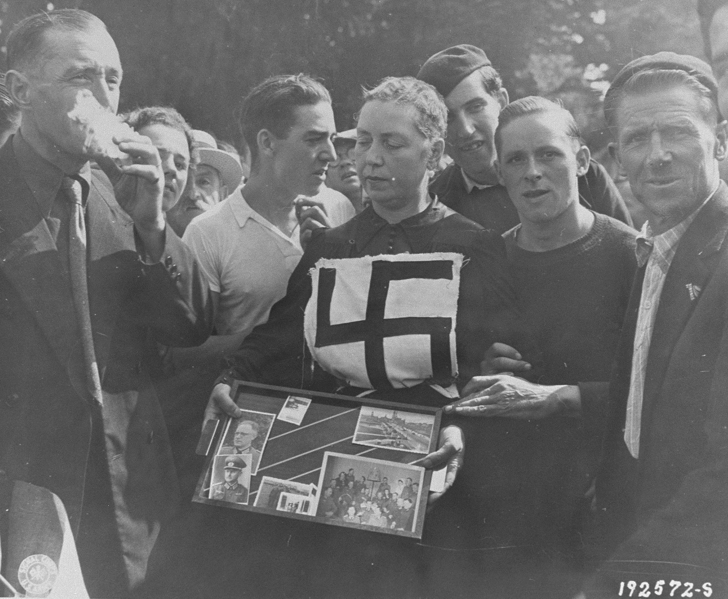 Members of the French resistance and citizens of Laval publicly humiliate a woman who consorted with a German officer during the occupation.  Her hair has been shorn and she has been marked with a swastika.  In addition, she is forced to display photographs of the German with whom she had a relationship.