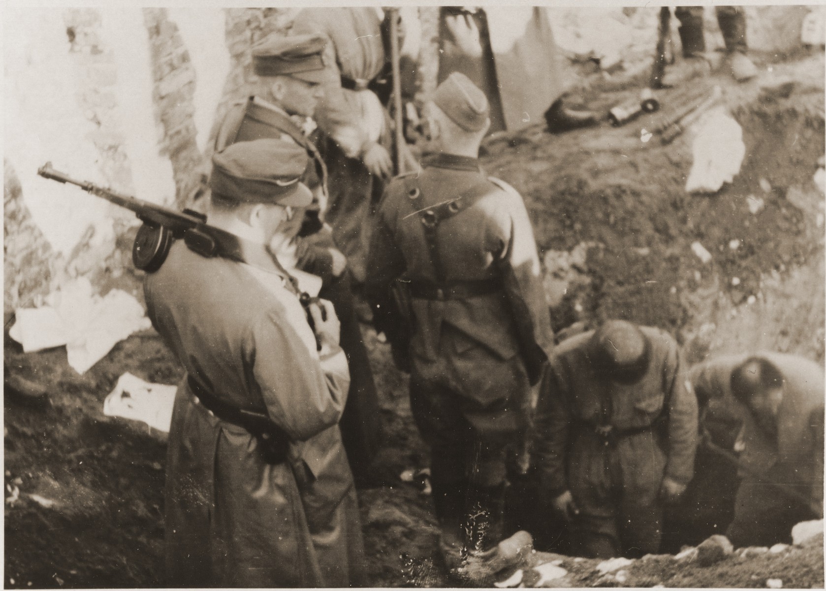 SS troops force Jews to dig out the entrance to a bunker on the twentieth day of the suppression of the Warsaw ghetto uprising.  The original German caption reads: "A bunker is opened."