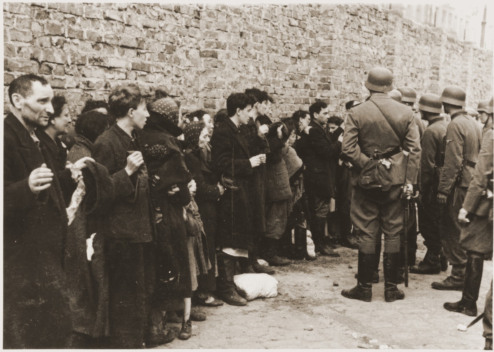 Jews captured by the SS during the Warsaw ghetto uprising are interrogated beside the ghetto wall before being sent to the Umschlagplatz.  The original German caption reads: "Search and Interrogation."