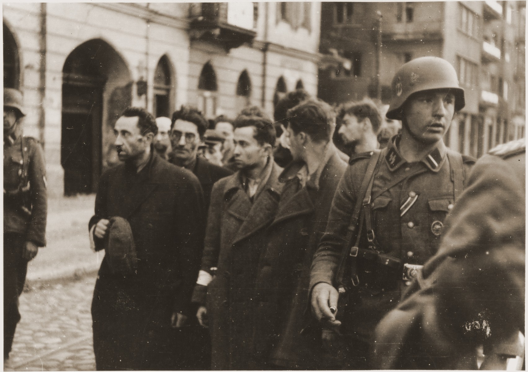 SS troops guard members of the Jewish resistance captured during the suppression of the Warsaw ghetto uprising.  

The original caption (translated from German) reads: "Bandits!"