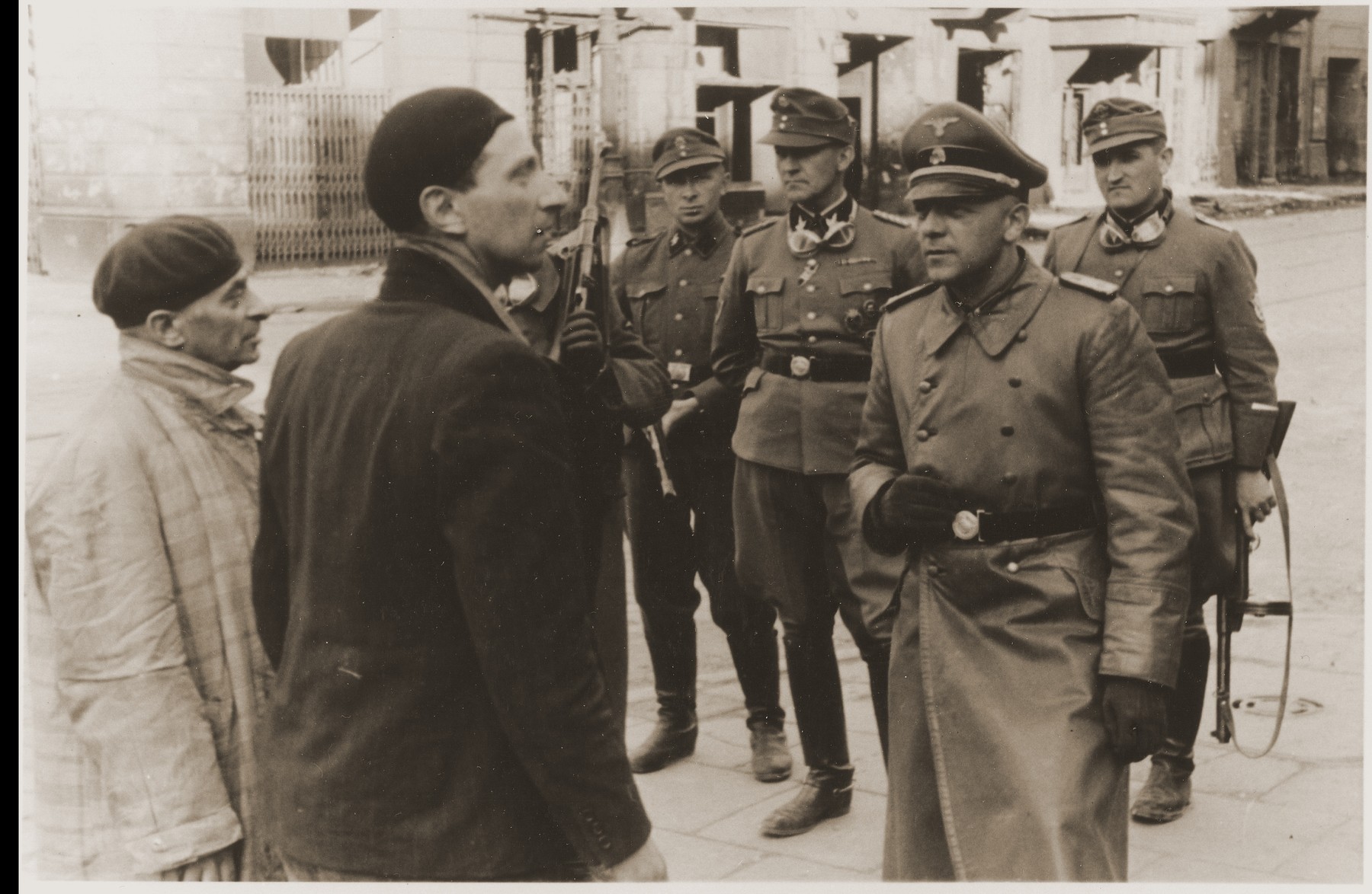 An SS officer questions two Jewish resistance fighters during the suppression of the Warsaw ghetto uprising, as SS-Brigadefuehrer Juergen Stroop (rear, center) and his security detail look on.

The original caption (translated from German) reads: "Jewish traitors."