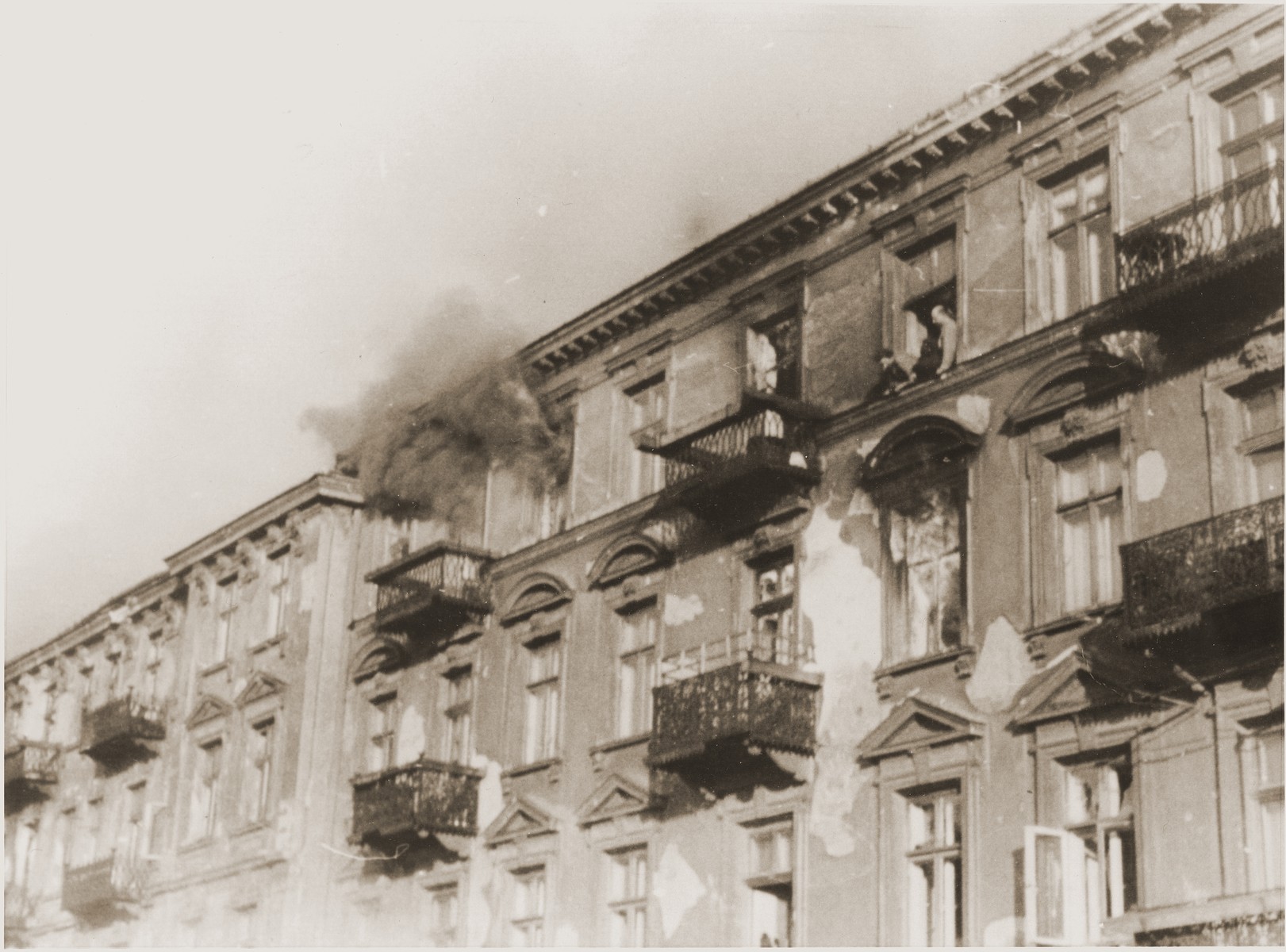 A man perched on the ledge outside of a fourth story window prepares to commit suicide by jumping rather than be captured by the SS on the fourth day of the suppression of the Warsaw ghetto uprising.  The original German caption reads: "Bandits jump to escape arrest."