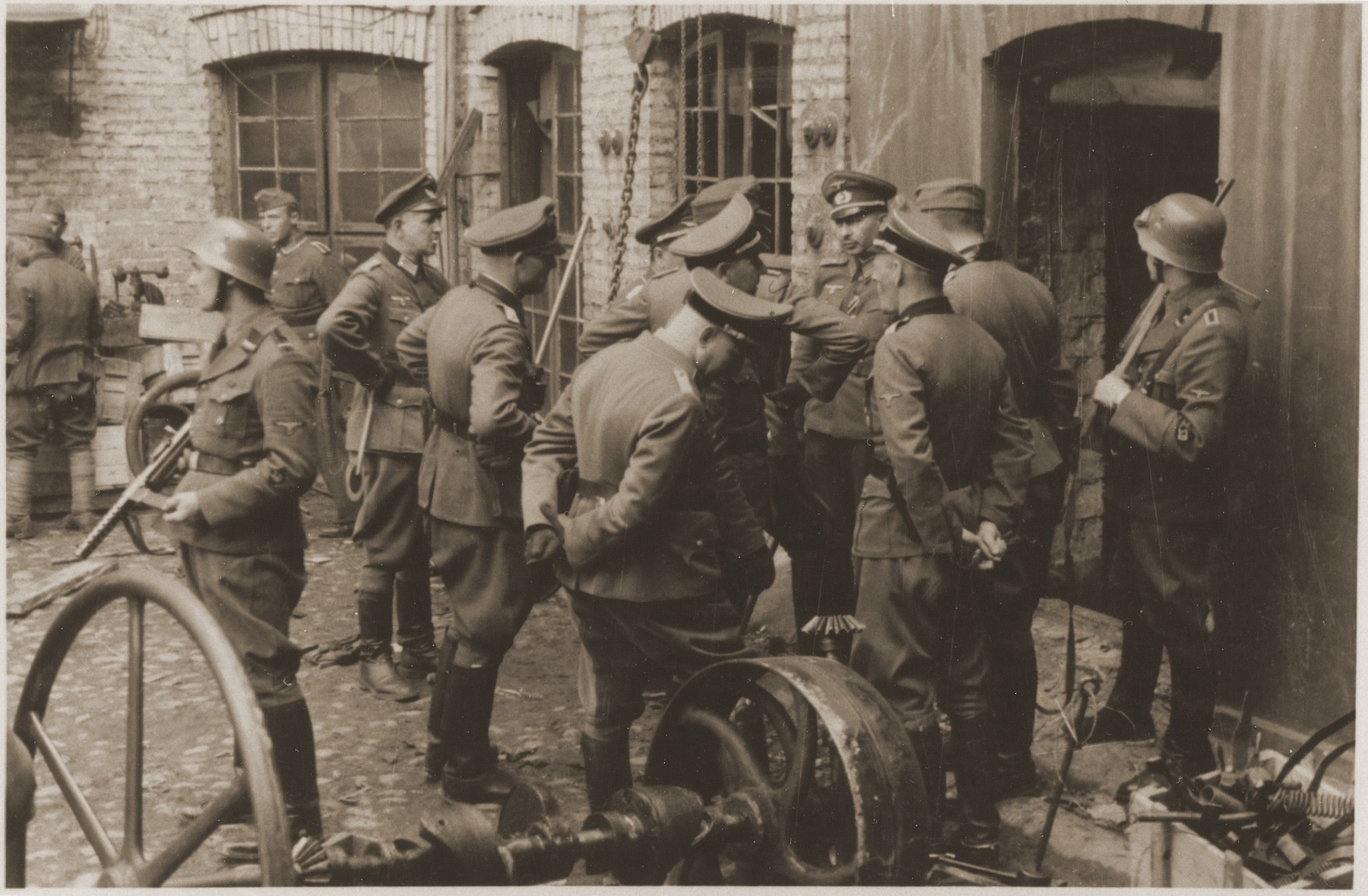 SS and German army officers, accompanied by SD guards, discuss the evacuation of a factory in the Warsaw ghetto during the uprising.  

The original caption reads: "Discussing the evacuation of an enterprise."