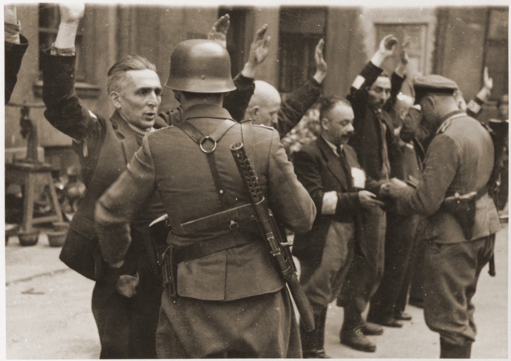 SS troops and officers search the Jewish department heads of the Brauer armaments factory during the suppression of the Warsaw ghetto uprising.  

The original German caption reads: "The Brauer firm."

Original caption from donated photograph reads:  "The following pictures are copies of the book conaning the report of the German commander who was responsible for cleaning out that ghetto in Warsaw, Poland.  This report, in the form of a leather bound book, was presented as evidence by the U.S. prosecution, Maj. Frank Walsh, at the international tribunal trials at Nurnberg, Germany."