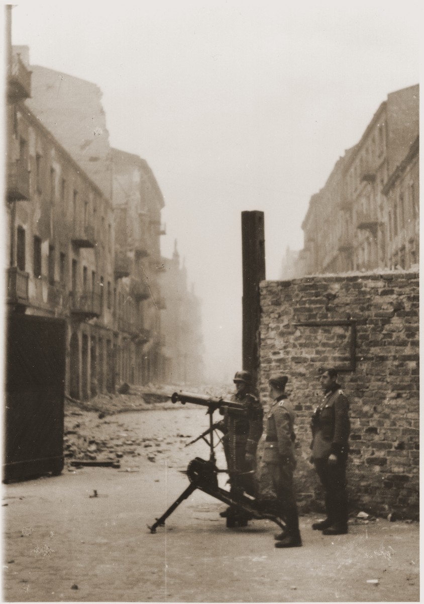 German police and an SS soldier man a machine-gun during the suppression of the Warsaw ghetto uprising.  

The original caption (translated from German) reads: "Securing a street."