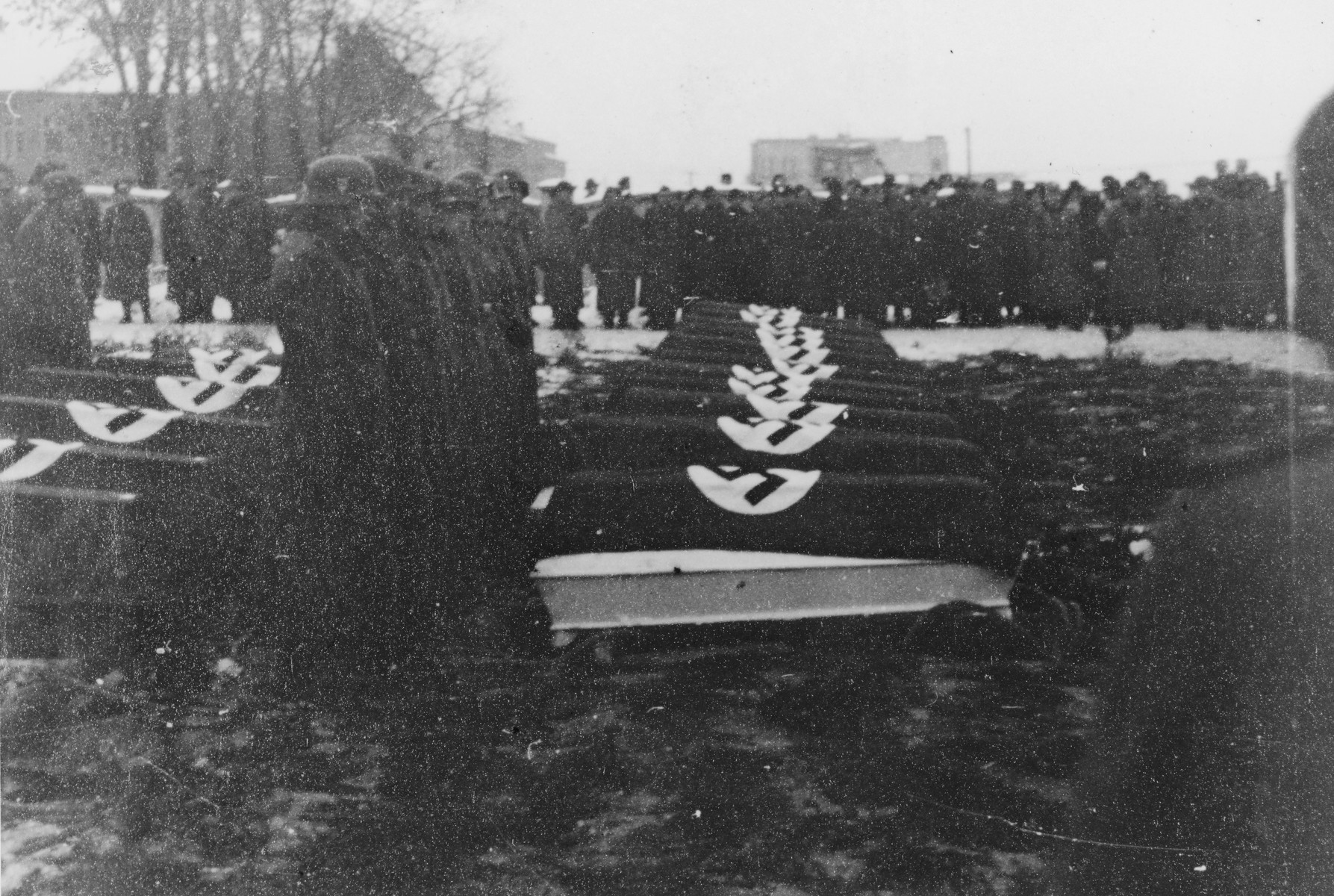 German troops stand at attention alongside a row of coffins during a military funeral near Auschwitz.

The original caption reads "Beisetzung von SS Kameraden nach einem Terrorangriff."  (Burying our SS comrades from a terror attack.)

[This probably is the aftermath of the December 26 bombing based on the snow on the ground but it could also be September 13th bombing of IG Farben in which 15 SS men died in the SS residential blocks and 28 were seriously wounded.]