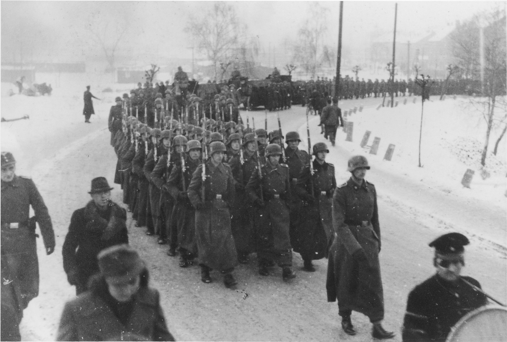 Germans troops in three long columns march along with rifles shouldered during a military funeral near Auschwitz.

The original caption reads "Beisetzung von SS Kameraden nach einem Terrorangriff."  (Burying our SS comrades from a terror attack.)

[This probably is the aftermath of the December 26 bombing based on the snow on the ground but it could also be September 13th bombing of IG Farben in which 15 SS men died in the SS residential blocks and 28 were seriously wounded.]