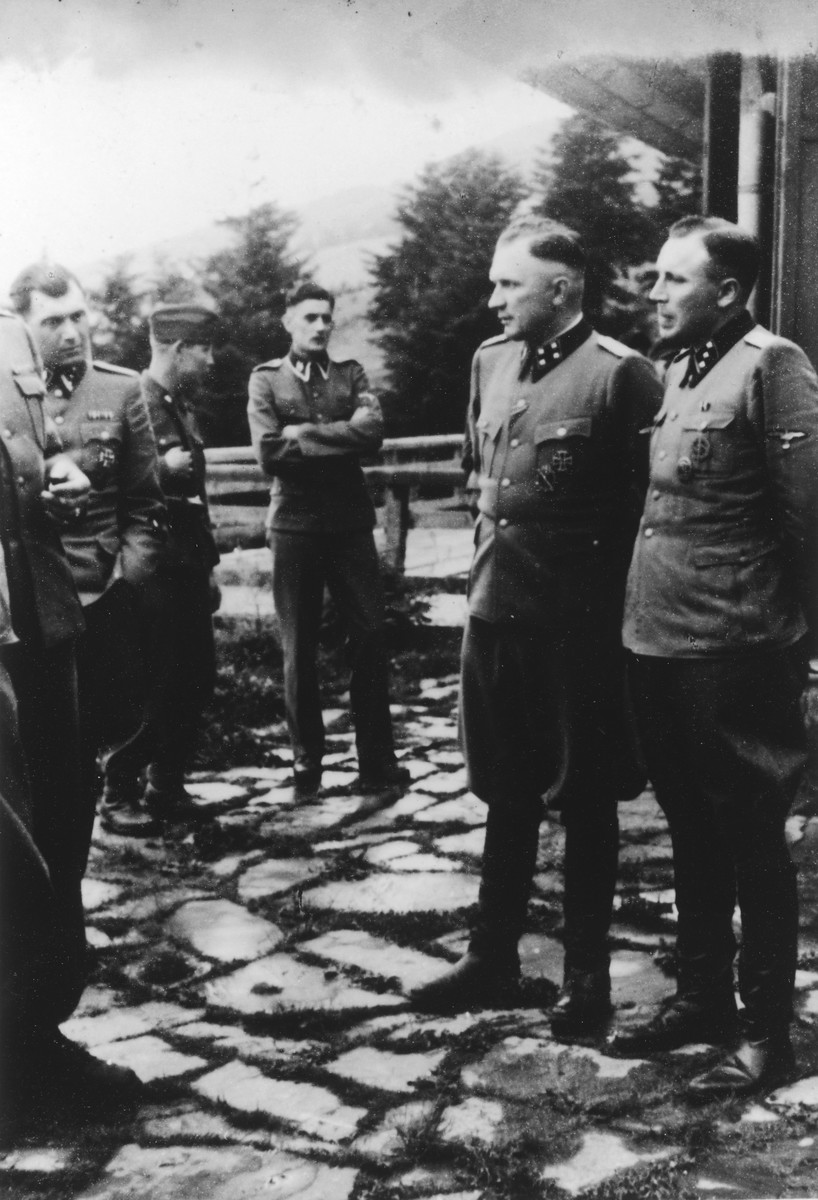Nazi officers stand on a terrace of Solahuette, the SS retreat outside of Auschwitz.

Pictured on the far left if Dr. Josef Mengele.  Pictured on the right are Commandant Richard Baer and his adjutant Karl Hoecker.

[Based on the officers visiting Solahutte, we surmise that the photographs were taken to honor Rudolf Hoess who completed his tenure as garrison senior on July 29.]