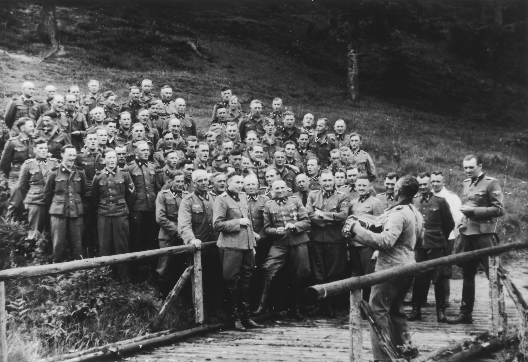 An accordionist leads a sing-along for SS officers at their retreat at Solahuette outside Auschwitz.

Pictured in the front row are Karl Hoecker, Otto Moll, Rudolf Hoess, Richard Baer, Josef Kramer (standing slightly behind Hoessler and partially obscured), Franz Hoessler, Josef Mengele, Anton Thumann, and Walter Schmidetzki.  Hermann Buch is in the center.  Konrad Wiegand, head of the Fahrbereitschaft (car and truck pool) is in the middle.

[Based on the officers visiting Solahutte, we surmise that the photographs were taken to honor Rudolf Hoess who completed his tenure as garrison senior on July 29.]