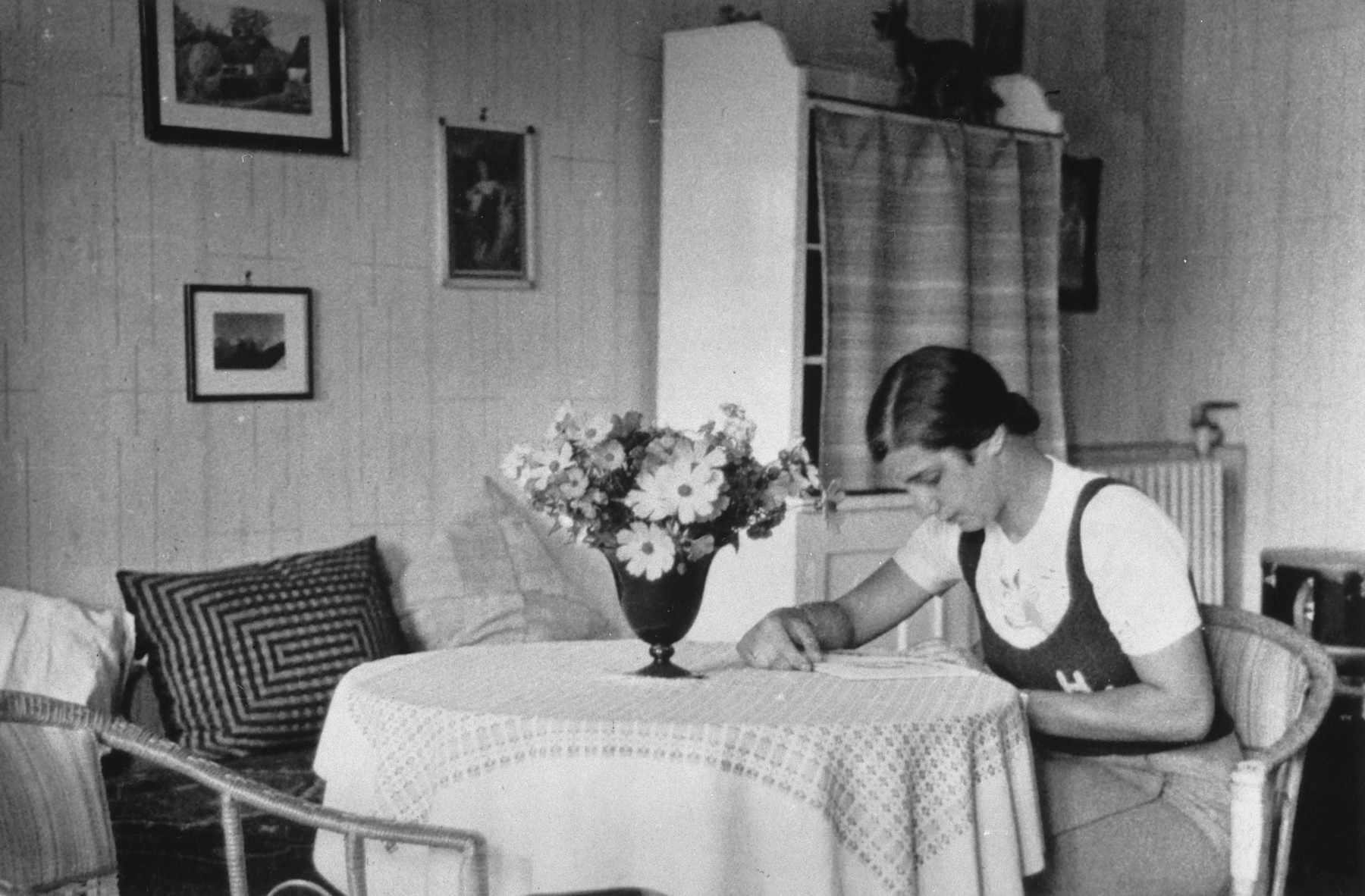A German-Jewish teenage girl sits at a table in her home and reads. 

Pictured is Hildegard Wolff.