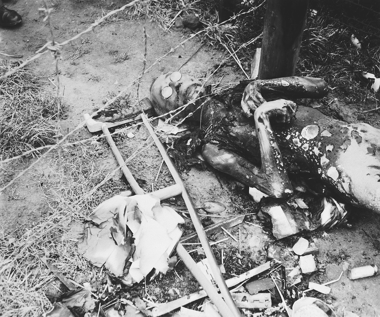 View of a badly burned corpse lying next to a barbed wire fence in the Leipzig-Thekla sub-camp.

The man's glasses are still on him and a crutch lies next to him.