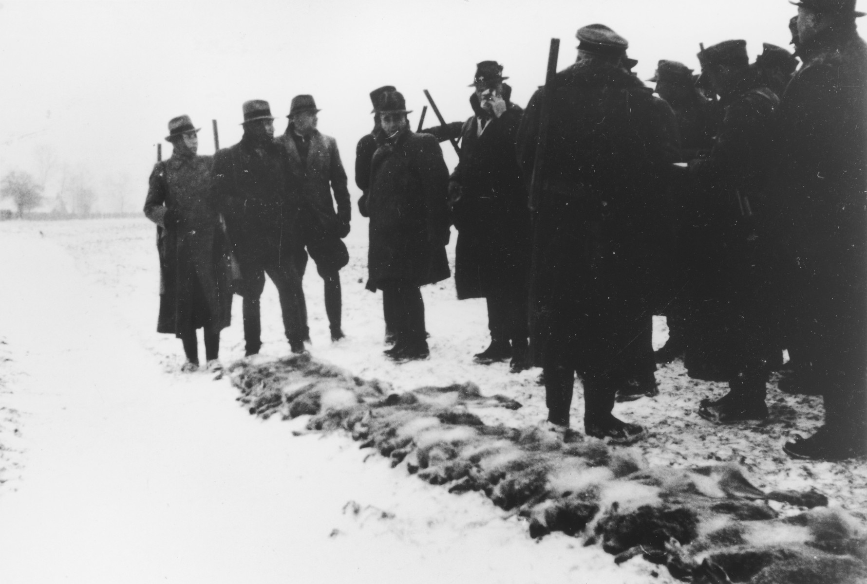 Several SS officers stand with their shotguns during a winter hunting excursion.  

The original caption reads "Treibjagd bei Schnee" (going hunting in the snow). 

Karl Hoecker is on the far left and Karl Moeckel is third from the left.