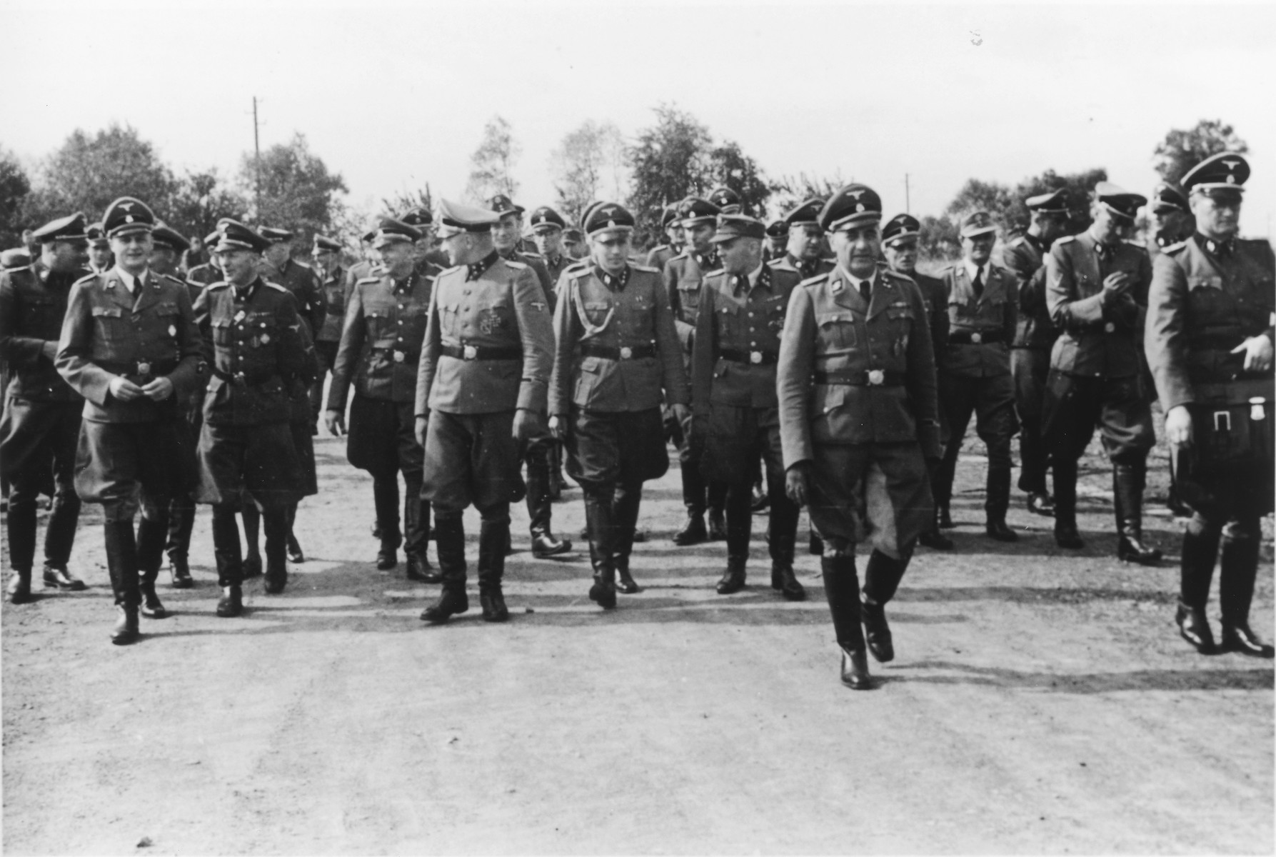 Nazi officers walk towards the dedication of the new SS hospital in Auschwitz.

The original caption reads "Besichtigung" (tour).

In the front (center left) is Karl Bischoff head of construction in Silesia.  Dr. Eduard Wirths is on the far left.  Next to him is Dr. Lolling.  Also pictured are Richard Baer, Karl Hoecker, Dr. Heinz Baumkoetter and Rudolf Hoess.