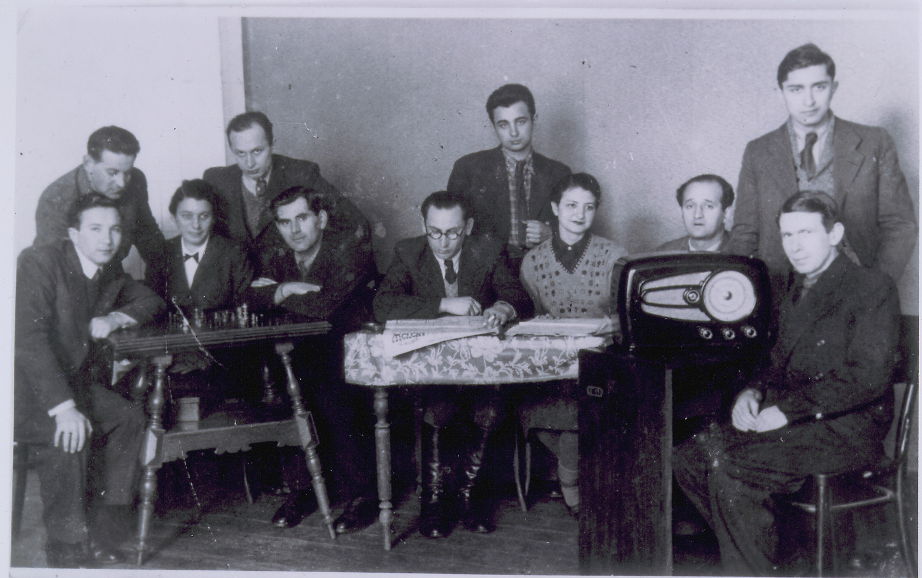 A group of refugee writers gather at the Internat Hostel in Vilna to read, play chess and listen to the radio. 

Mozes Segal stands at the center.