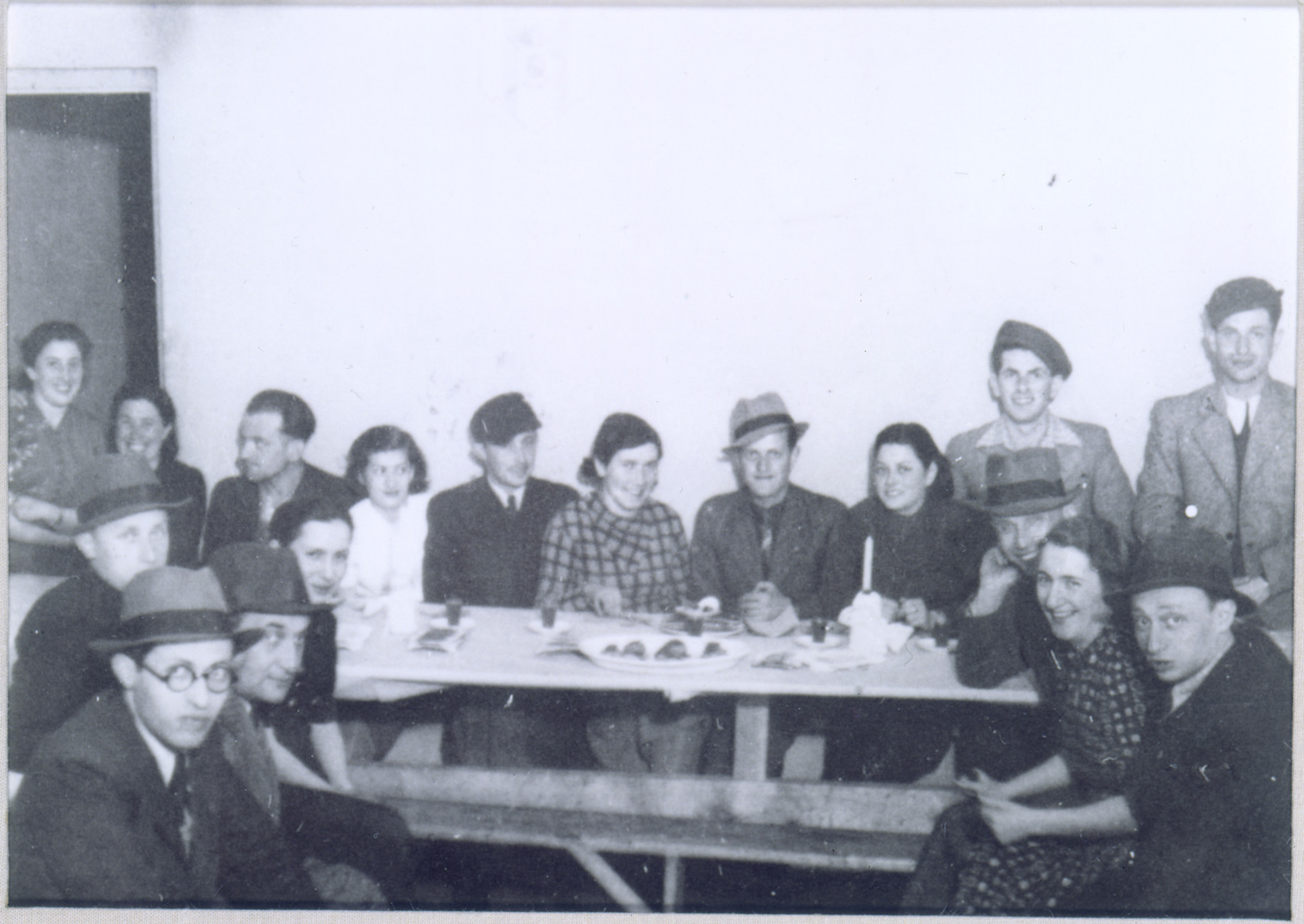 Gathering of Polish Jewish refugees at the "Internat" Betar youth hostel in Vilna.  

Among those pictured are Menahem Begin (at the front left); Fejga Szepsenwol (top left); and Chaya Szepsenwol (third from the right, behind the candle).  Pictured on the right are probably Batya and Israel Scheib (Eldad), future leader of the Lechi.

The Internat was one of a series of communal residences established by the American Jewish Joint Distribution Committee to help deal with the housing crisis that resulted when thousands of Polish Jewish refugees flooded into Vilna in the months following the outbreak of WWII.  The JDC grouped the refugees (who were largely unaccompanied youth) in residences according to youth movement affiliation.