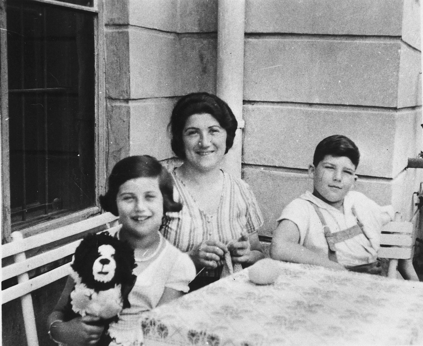Portrait of an Austrian-Jewish family sitting around an outdoor table.

Pictured from left to right are Susi, Olga, and Herbert Popper.
