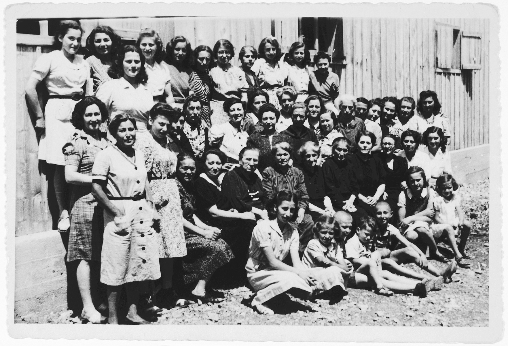 Group portrait of female and child prisoners standing and sitting outside a barrack in the Kraljevica concentration camp.

Among those pictured are Nada and Lea Gostl, school friends of the donor. Also pictured are Mira and Zora Mahler and their mother, Luisa Mahler.