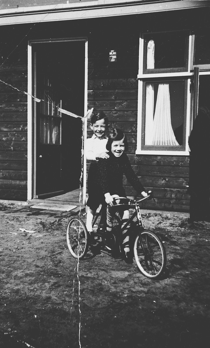 Two Jewish children share a bicycle outside one of the barracks in the Westerbork internment camp.

Pictured on the left is Michael Fink.