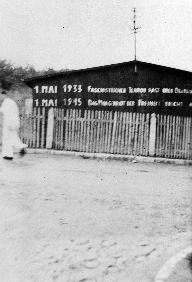 A survivor walks past a sign on the exterior of a barrack in the Buchenwald concentration camp describing the significance of May 1 in both the years 1933 and 1945.
