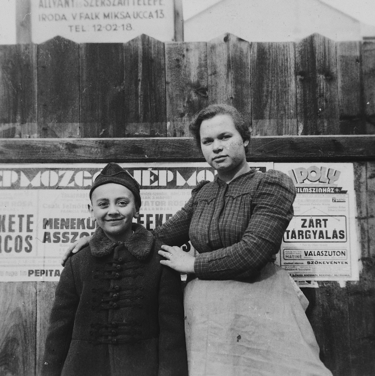 A young Jewish boy poses with his Hungarian nanny in front of a poster tacked on a wooden fence in Budapest.

Pictured is Ivan Pal.