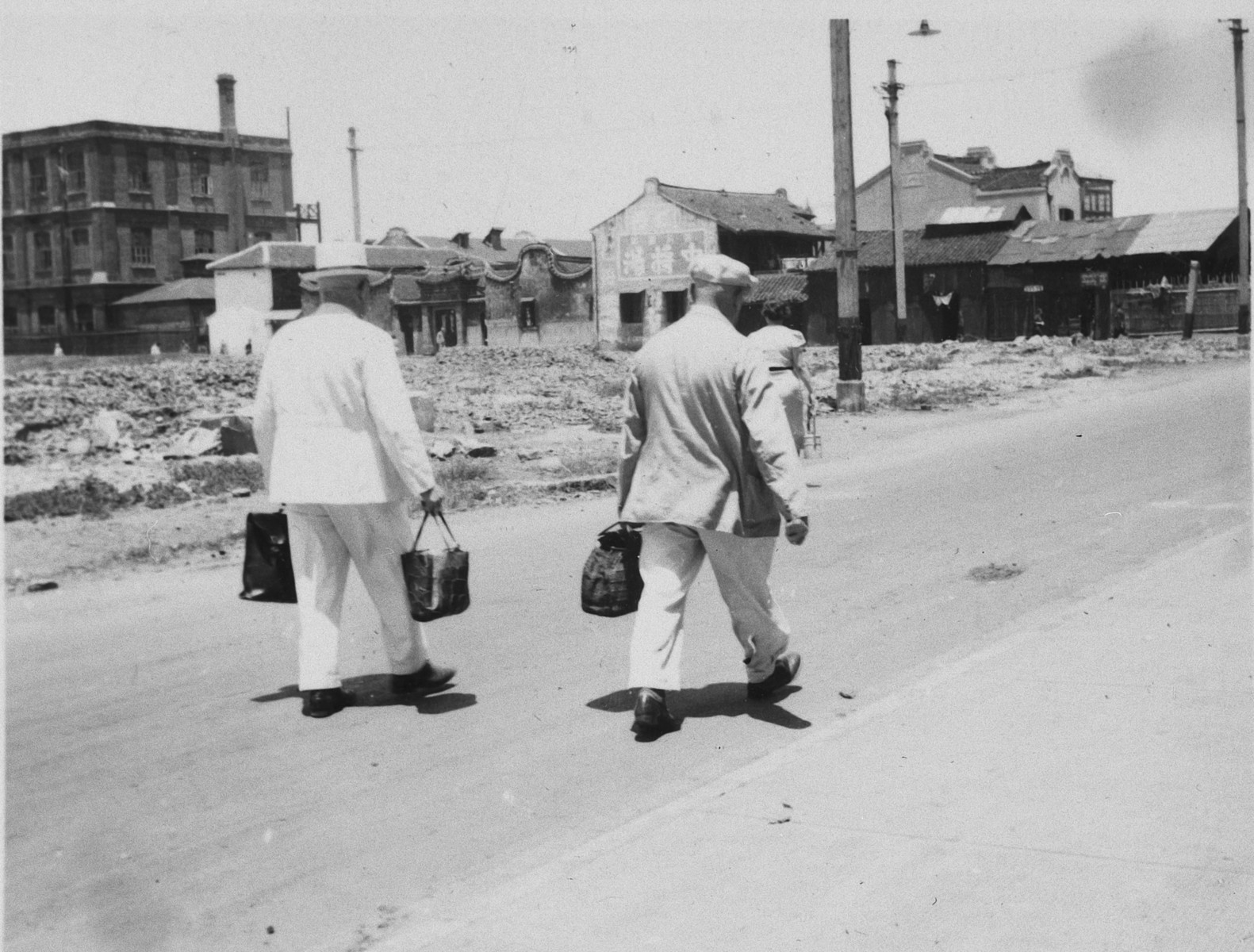 Two men walk down a street in Shanghai carrying packages of food. 

The original caption reads "Das Essen wird nach Hause getragen."