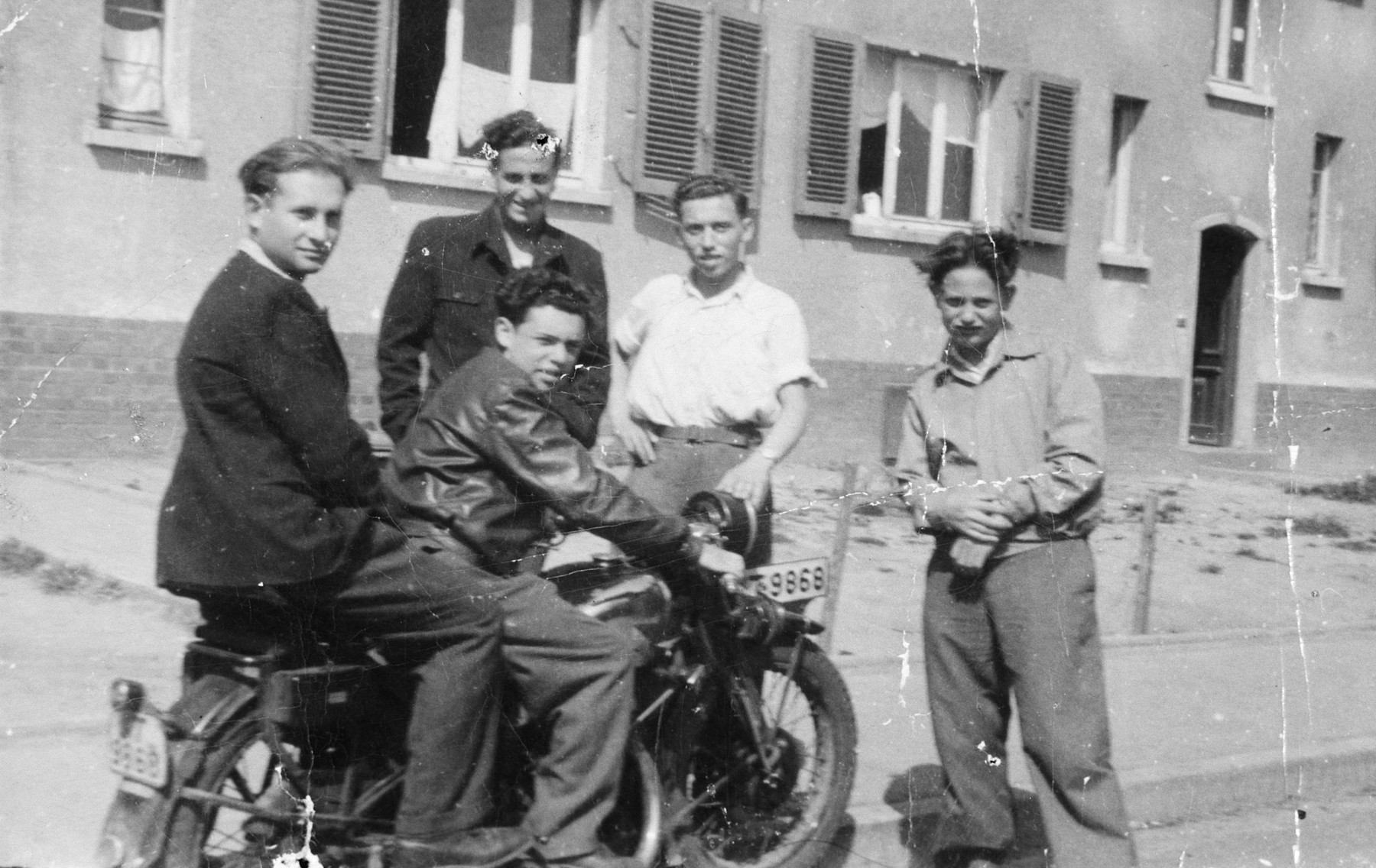 Five young men pose on or next to a motorcycle in the Zeilsheim displaced persons' camp.

Standing second from the left is Chuna Grynbaum.  Alex Herblum is on the motorcycle.