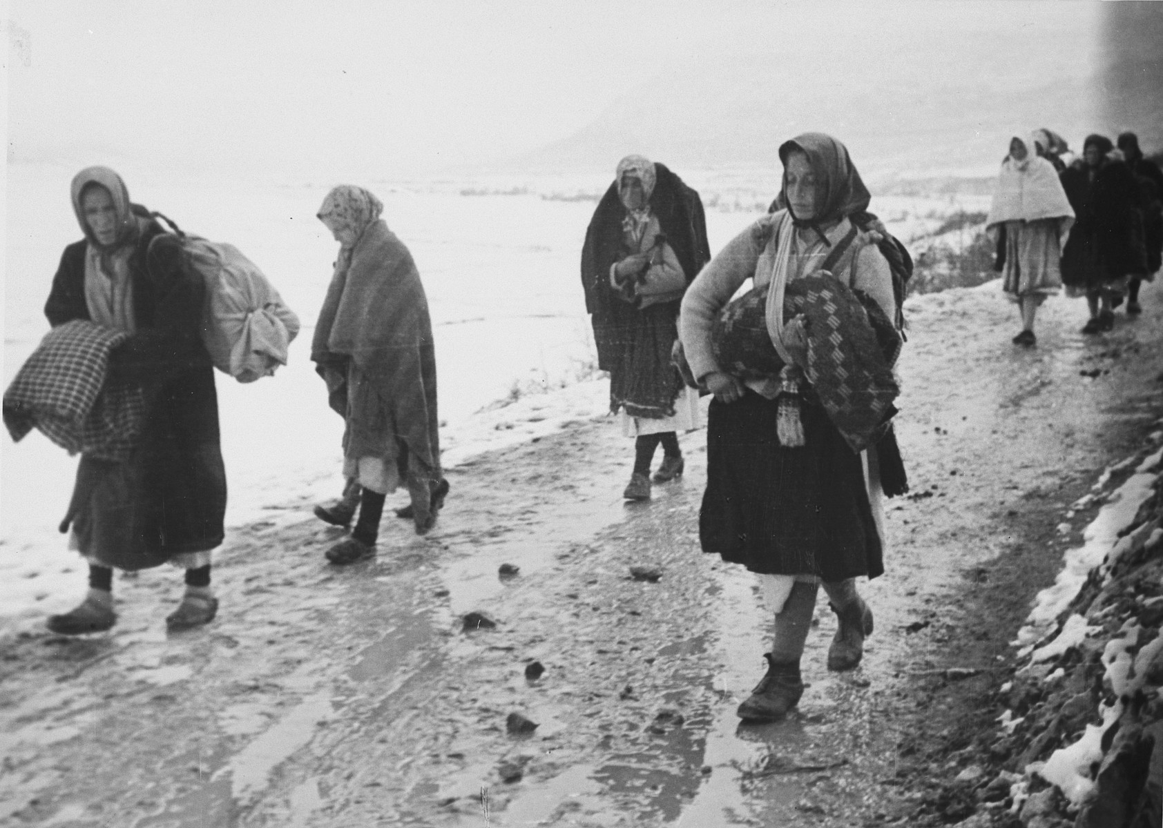Female refugees walk down a path in Croatia, carrying their belongings. 

The original Waffen-SS caption reads,  "Fluechtlinge, die von den Partisanen gewaltsam mitgeschleppt wurden, kehren in ihre Heimat zurueck."  (Tranlsated, "Refugees, who were forcibly carted off by partisans, return to their homes."

One of a series of photographs taken by the 7th SS Volunteer Mountain Division Prinz Eugen in Croatia, Serbia, and Montenegro from 1942 to 1944, after the German invasion of the Kingdom of Yugoslavia. The photographs are believed to have been captioned by the commanding office of the Waffen-SS, and had been in the possession of  Friedrich Wilhem Krueger, who served with the division from November 1943 until April 1944.