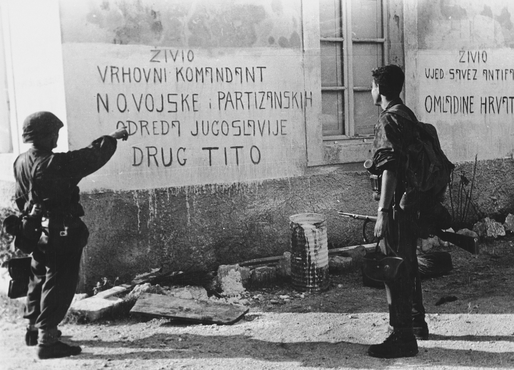 Soldiers of the Prinz Eugen Division point to writing on the front of a house with a graffiti on it ("Zivio Vrhovni Komandant N.O.Vojske; Partizanskih Odreda Jugoslavije Drug Tito"). 

The original Waffen-SS caption reads, "Einsatz an der Adria. Aufschriften auf einem vom Feind nun verlassenen Gemeindehaus."  (Tranlsated, "Action near the Adria. Capturing a community house, which was left by the enemy."

One of a series of photographs taken by the 7th SS Volunteer Mountain Division Prinz Eugen in Croatia, Serbia, and Montenegro from 1942 to 1944, after the German invasion of the Kingdom of Yugoslavia. The photographs are believed to have been captioned by the commanding office of the Waffen-SS, and had been in the possession of  Friedrich Wilhem Krueger, who served with the division from November 1943 until April 1944.