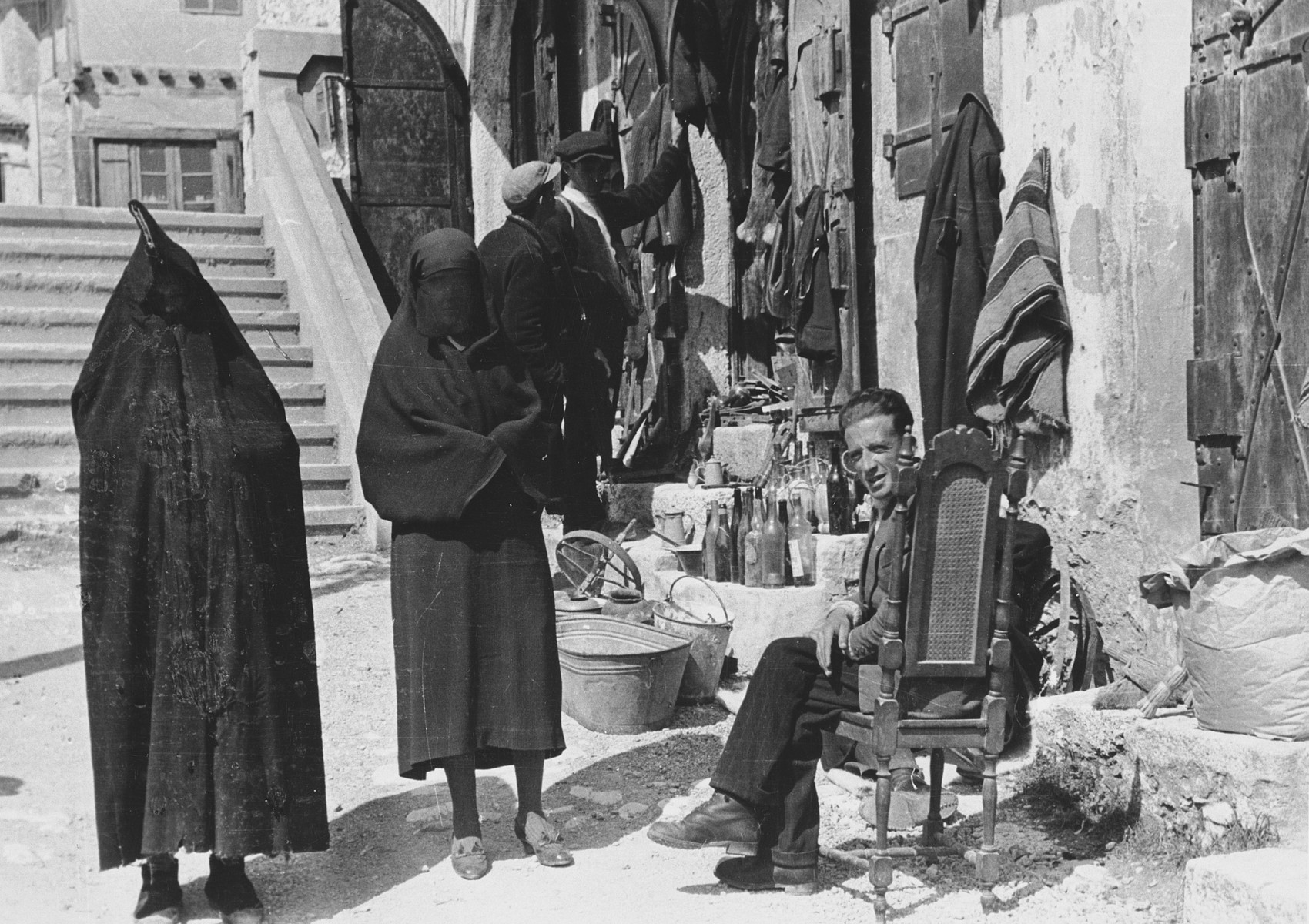 Two veiled women walk past a small shop on a street in Mostar. 

The original Waffen-SS caption reads, "Fruehere Hauptstrasse in Mostar."  (Tranlsated,  "Former mainstreet in Mostar.")

One of a series of photographs taken by the 7th SS Volunteer Mountain Division Prinz Eugen in Croatia, Serbia, and Montenegro from 1942 to 1944, after the German invasion of the Kingdom of Yugoslavia. The photographs are believed to have been captioned by the commanding office of the Waffen-SS, and had been in the possession of  Friedrich Wilhem Krueger, who served with the division from November 1943 until April 1944.