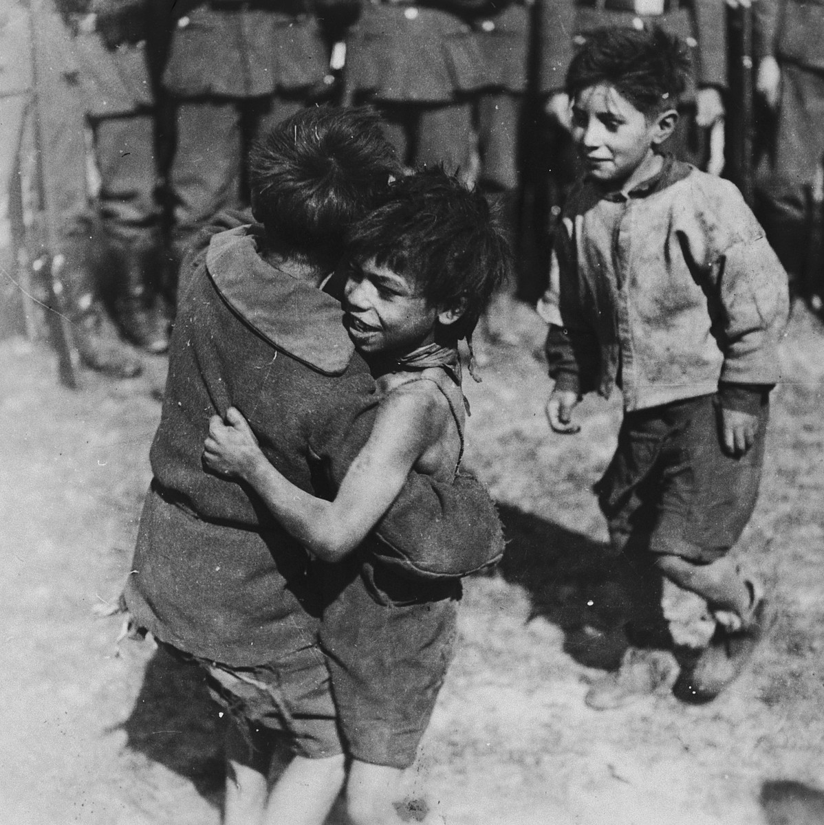 Two young Romani children embrace while a third looks on.