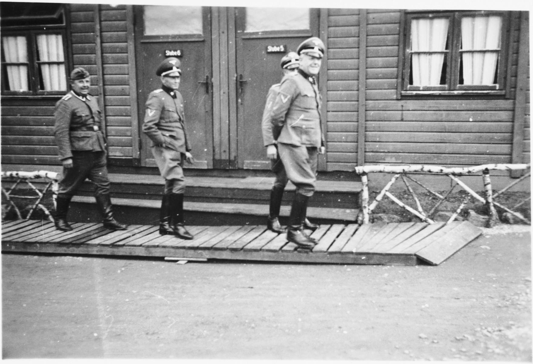 Commandant Hermann Pister, accompanied by three other officers, exits a wooden building (possibly an administrative barracks)  at Hinzert (a sub-camp of Buchenwald).

Pictured in the center is Anton Ganz.