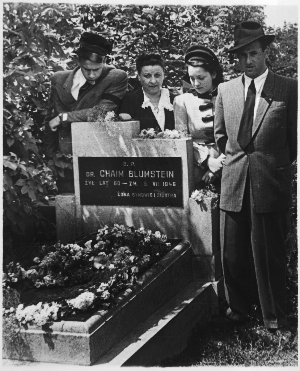 Family portrait of a Yahrzeit in post war Poland.

Pictured are Alexandre Blumstein (far left), Estera Blumstein, Hela Blumstein and Nataniel Blumstein.

This photograph, taken on July 6, 1947, shows the Yahrzeit of Chaim Blumstein.  His family visits his grave in commemoration of his death as suggested by Jewish tradition.  This visit was one of the last before the remaining family members pictured here emigrated from Poland to Paris, France.