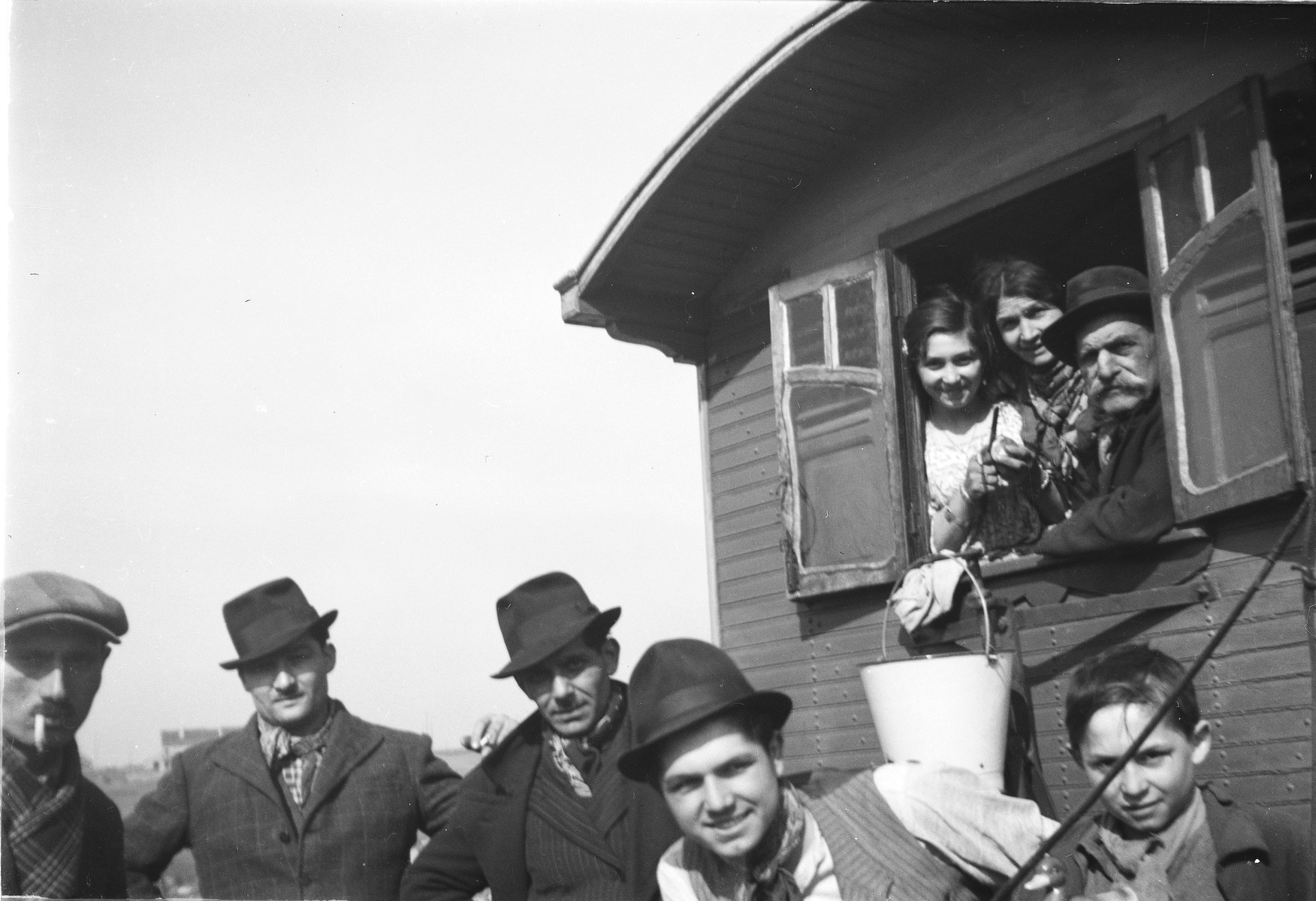 A Romani family poses by their caravan, some standing outside and others looking out from the window. 

Pictured on the bottom, second from the right is Yayal (last name unknown).