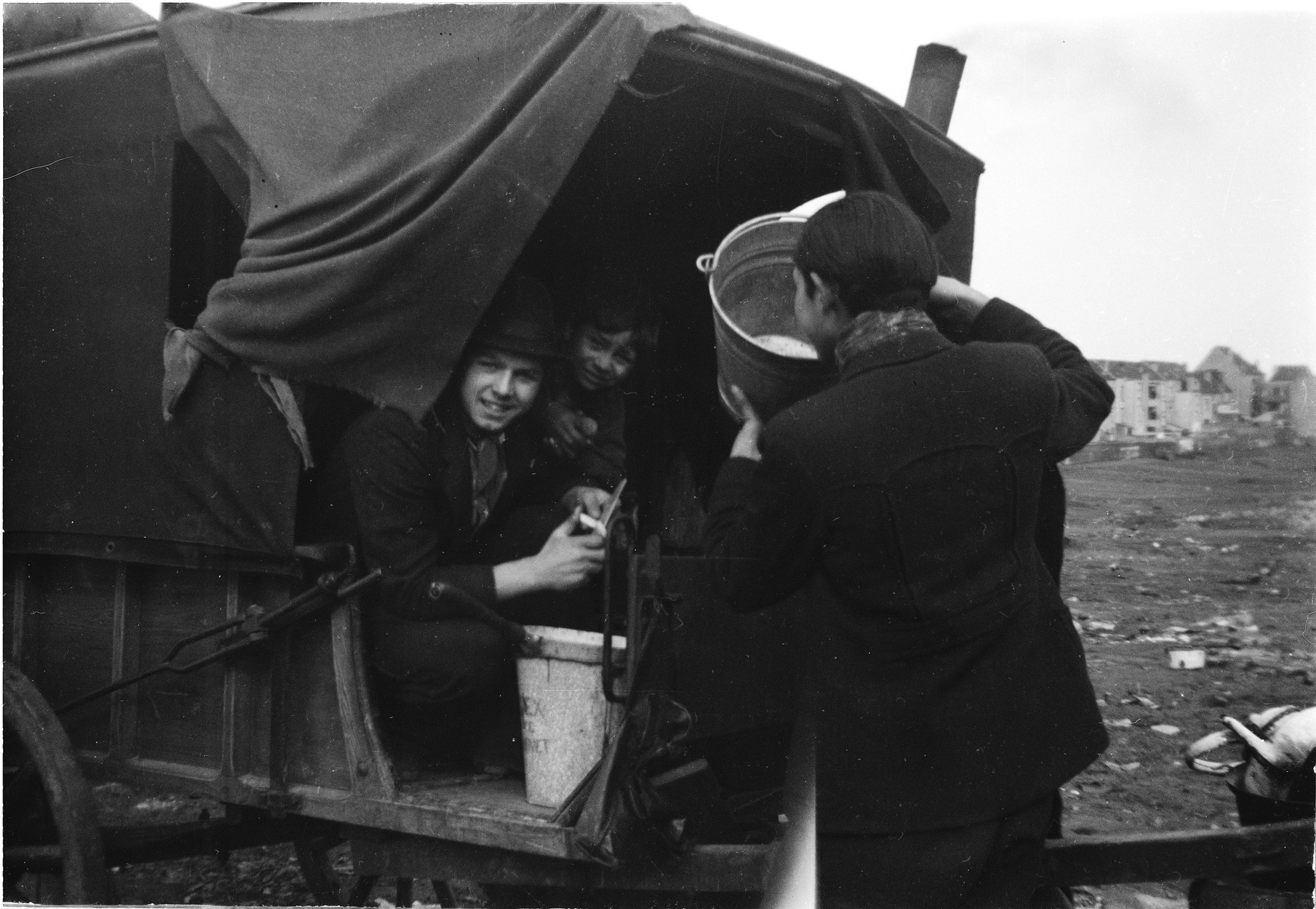 Two Romani women seated in their caravan work with a Romani man, who is lifting a  bucket.