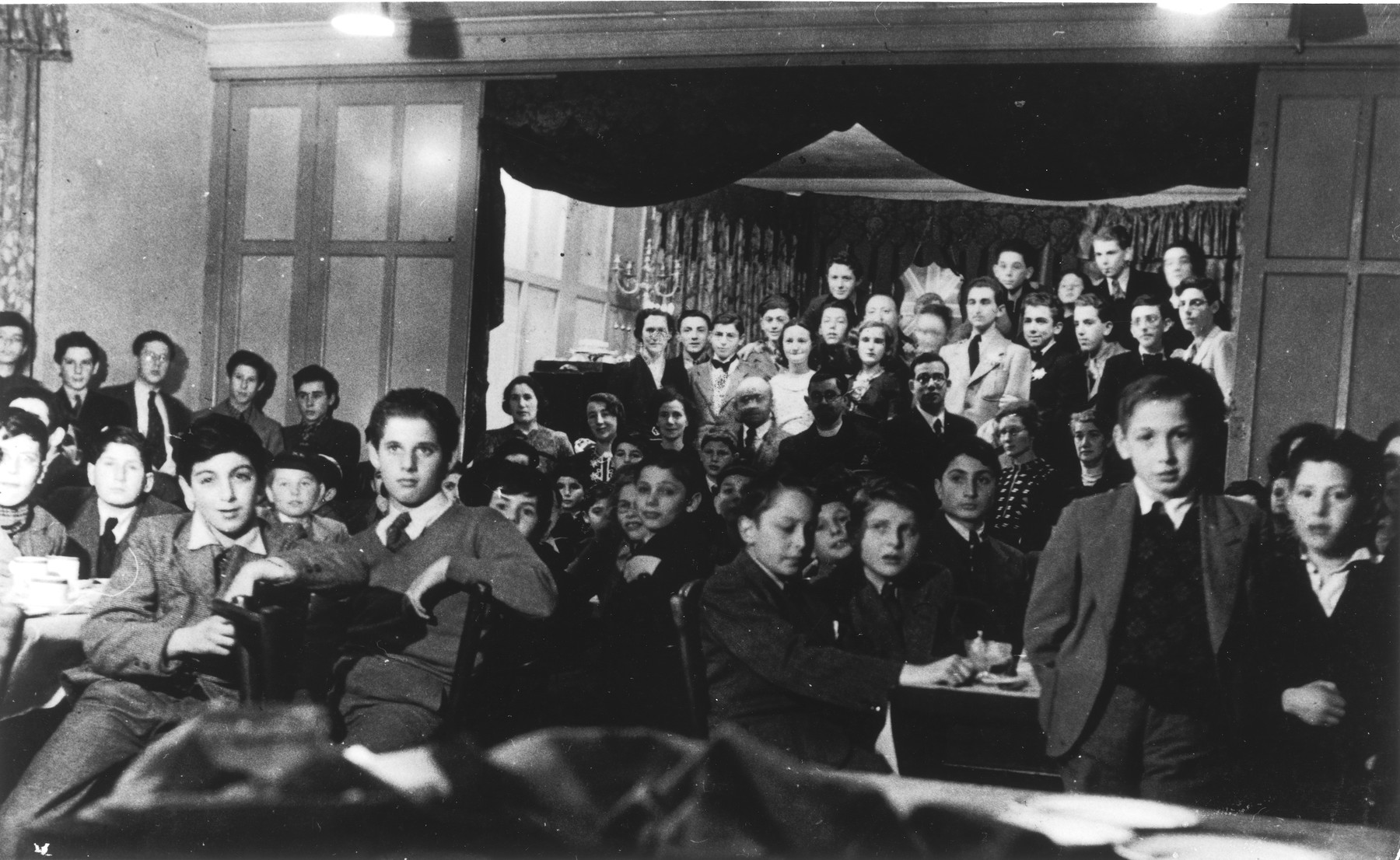 Jewish children from the Rowden Hall School attend a Hannukah party in an overflow hostel on Harold Road.

Among those pictured are Guenther Cahn, his brother Helmuth Cahn (later Harry Curtis), Eric Hamburger, Kurt Berger ( a teacher recruited from the internees in the Kitchener Camp), Mr. and Mrs. Katz and Mrs. Bergel.