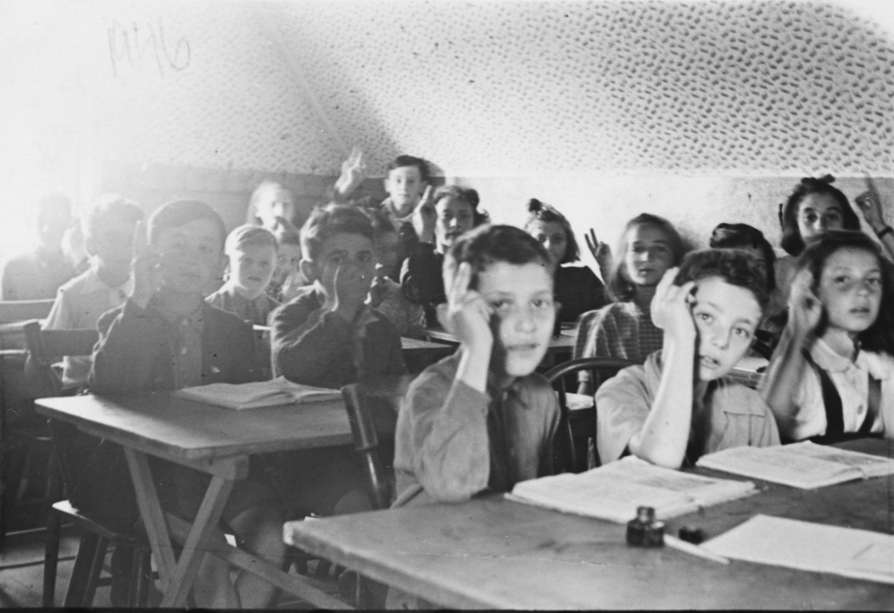 Children sit at their desks and raise their hands in a school in the ...