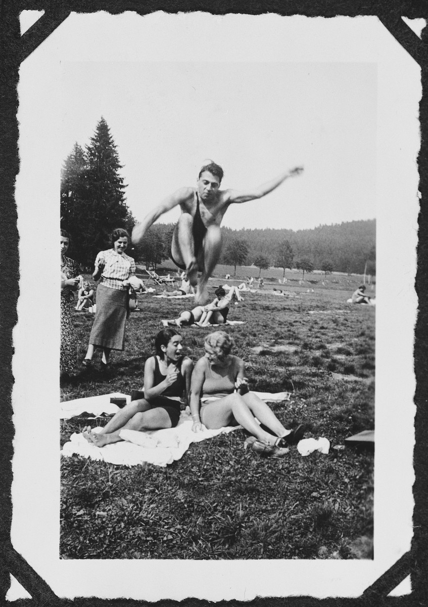 Heinz Bähr leaps over his cousin and a friend during an outing to a park in or near Freiburg.

Seated on the towel is Margot Bähr (left).  Her sister  Ruth is watching on the far left.