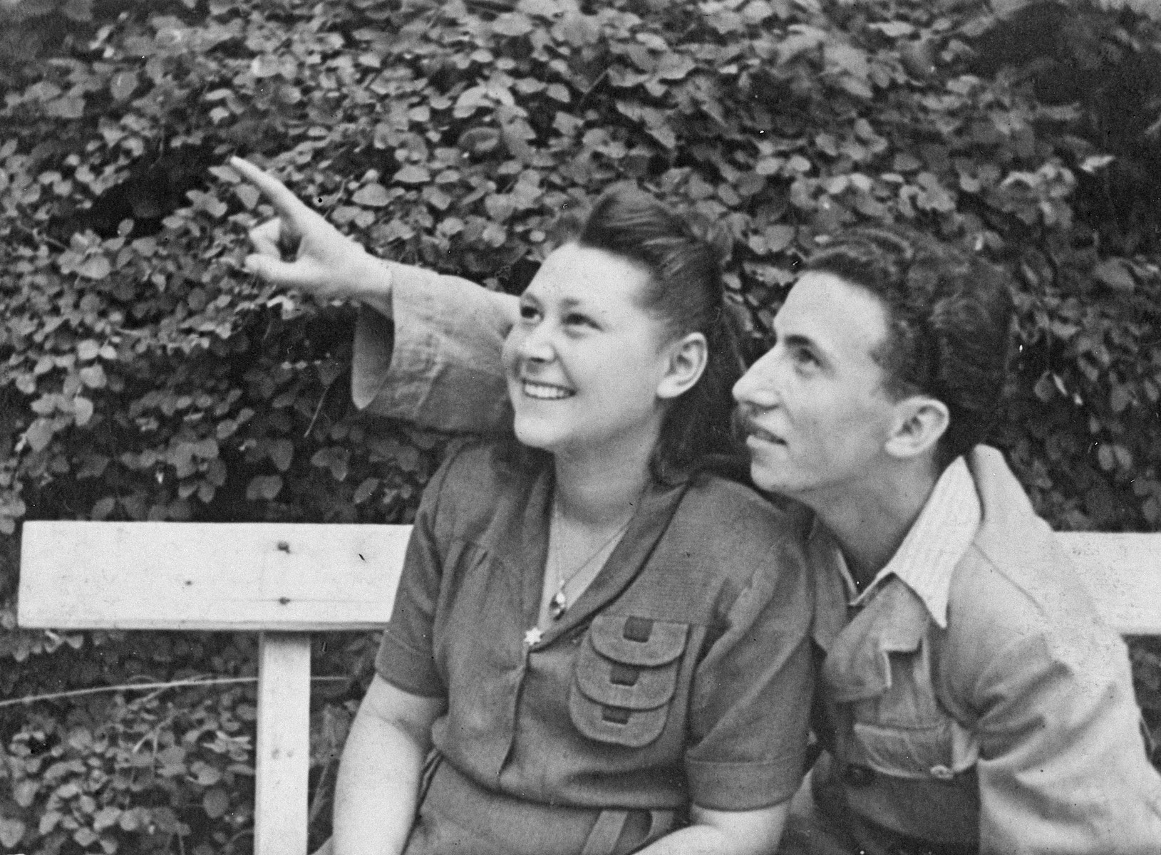A young couple sits on a bench in the Leipheim DP camp and looks up at something in the sky.

Pictured are Rachel and Lolek Grynfeld.